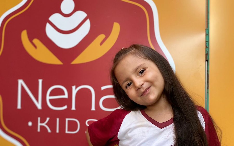 Aluna do Colégio Nena Kids em frente à logo da escola